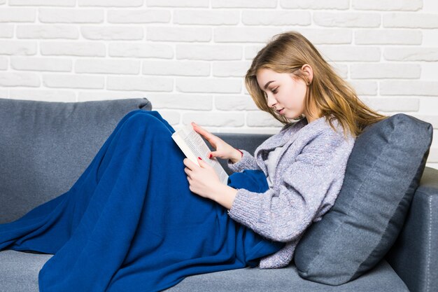 Cerca de mentira jovencita leyendo libro relajante en casa