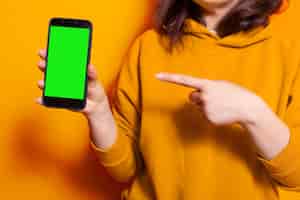 Foto gratuita cerca de una mujer apuntando a una pantalla verde vertical en el teléfono. persona que tiene una plantilla de maqueta aislada y un fondo con clave de croma en el teléfono inteligente. adulto con teléfono móvil en cámara