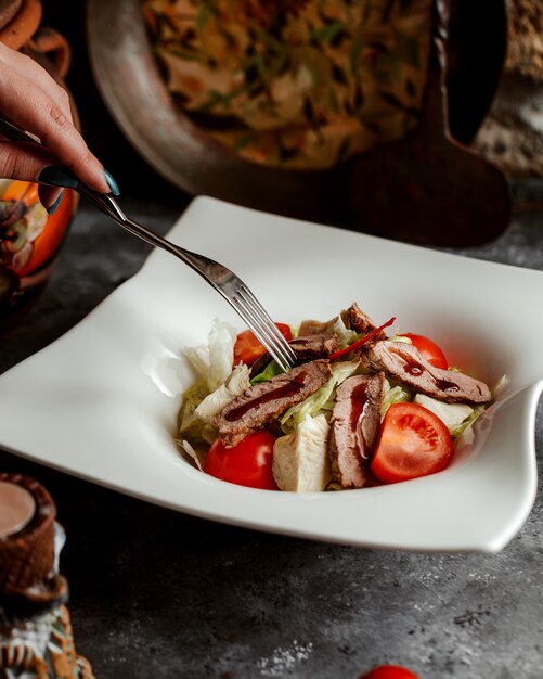 Cerca de mujer comiendo ensalada de carne con lechuga, tomate y salsa