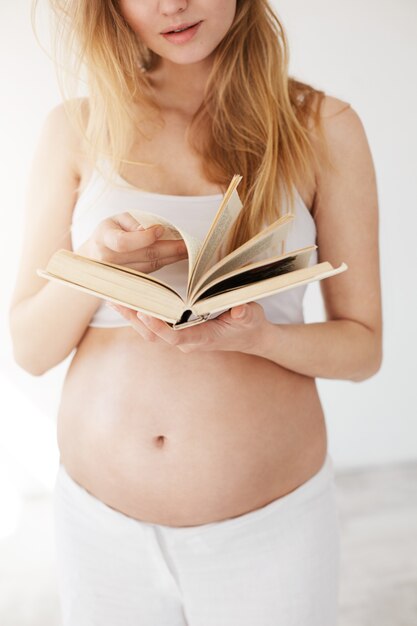 Cerca de una mujer embarazada leyendo un libro sobre bebés y familia.