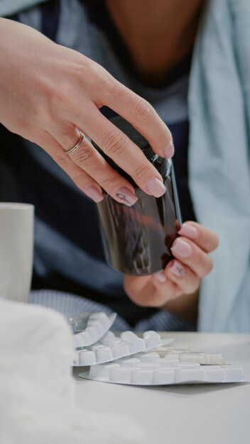 Cerca de mujer leyendo etiquetas de tabletas y frascos con píldoras y cápsulas en la mesa con medicamentos, tejidos y termómetro. Persona enferma que busca tratamiento para curar los síntomas del virus.