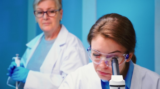 Cerca de la mujer médico químico que trabaja en el laboratorio científico equipado con microscopio