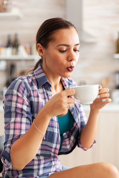 Cerca de mujer sosteniendo una taza de té verde caliente tratando de beberlo