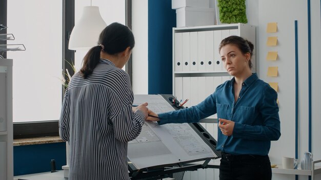 Cerca de mujeres analizando el modelo de construcción y la estructura de la maqueta para diseñar el plan de planos. Equipo de arquitectos trabajando en proyecto de construcción arquitectónica y desarrollo urbano.