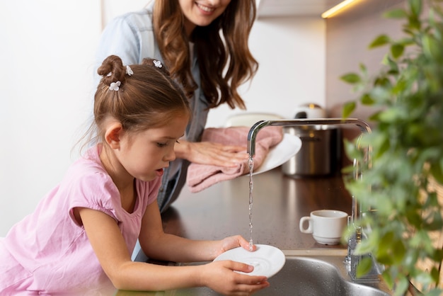 Cerca de niña ayudando a su mamá con platos