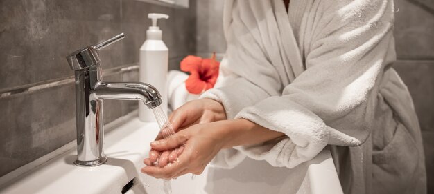 Cerca de una niña en bata de baño se lava las manos en el baño.