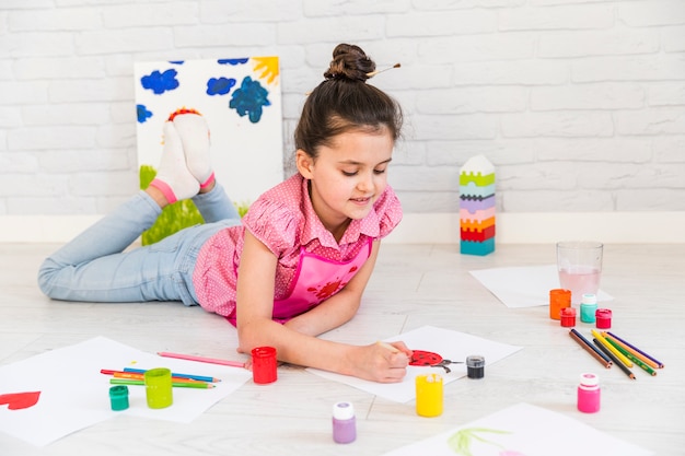 Cerca de una niña tendida en el suelo pintando la mariquita sobre papel blanco