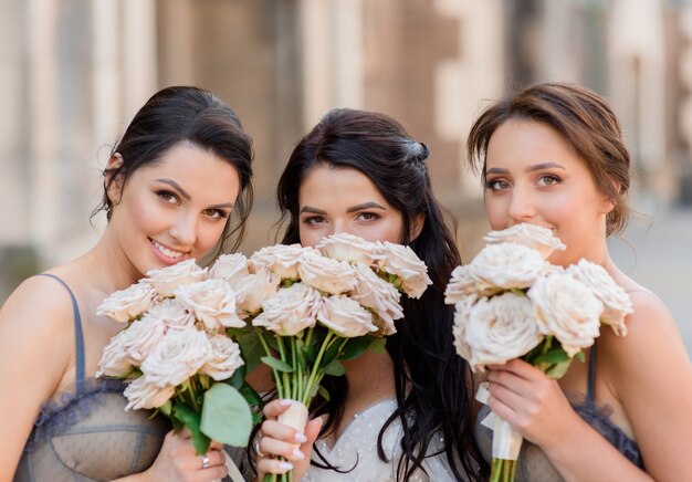 Cerca de la novia morena junto con las damas de honor entierran sus rostros detrás de los ramos de novia y miran a la cámara