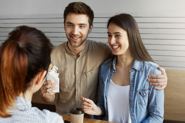 Foto gratuita cerca de un par de jóvenes estudiantes sentados en la cafetería después del estudio, hablando sobre la graduación y los planes para el futuro. chico guapo abrazando a su novia.