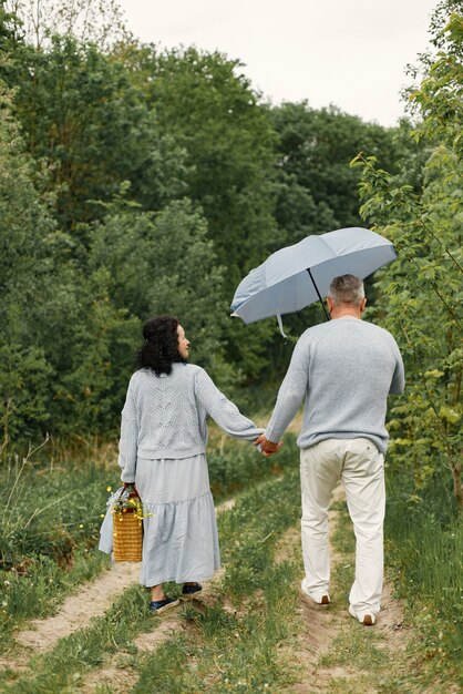 Cerca de una pareja romántica caminando en un parque de otoño. Hombre y mujer vistiendo suéteres azules. Hombre que sostiene un paraguas.