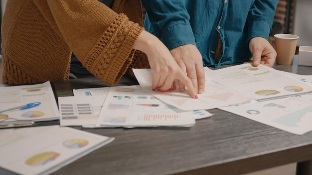 Cerca de personas revisando papeles con gráficos de tasas de datos en la mesa. Compañeros de trabajo mirando archivos para planificar proyectos comerciales y estrategias de marketing. Colegas trabajando en la presentación.