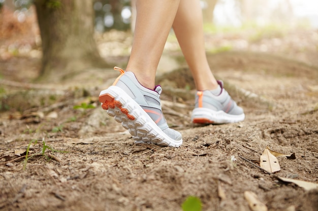 Cerca de las piernas en forma de joven atlética con zapatos para correr mientras se ejecuta en la pista forestal. Vista trasera de la corredora haciendo ejercicio al aire libre, preparándose para un maratón serio.