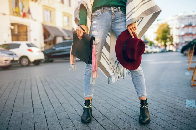 Cerca de las piernas de la mujer con botas de cuero negro, jeans, tendencias de primavera de calzado, bolsa de sujeción