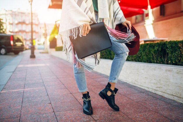 Cerca de las piernas de la mujer con botas de cuero negro, jeans, tendencias de primavera de calzado, bolsa de sujeción