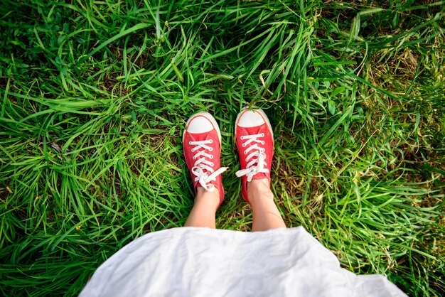 Cerca de las piernas de la niña en zapatos rojos sobre hierba