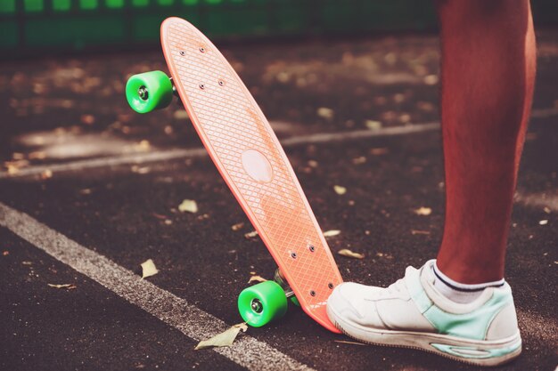 Cerca de pies de hombre zapatillas monta en patineta centavo naranja sobre asfalto