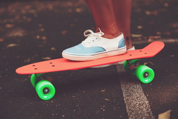 Cerca de los pies de las zapatillas de niña monta en patineta centavo naranja sobre asfalto