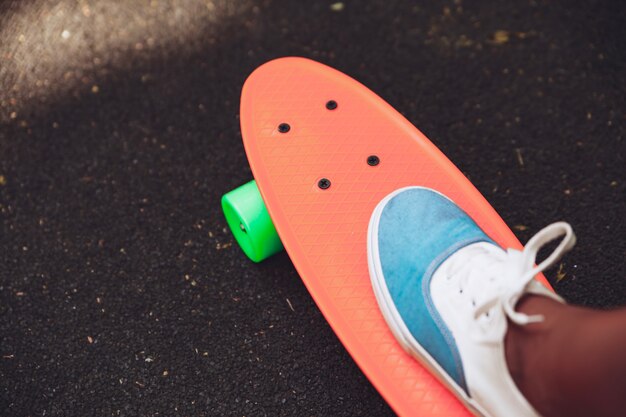 Cerca de los pies de las zapatillas de niña monta en patineta centavo naranja sobre asfalto