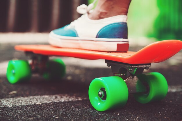 Cerca de los pies de las zapatillas de niña monta en patineta centavo naranja sobre asfalto