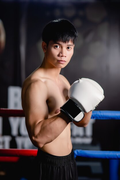 De cerca, retrato joven apuesto en guantes de boxeo blancos pose de pie sobre lienzo en el gimnasio, clase de boxeo de entrenamiento de hombre sano,