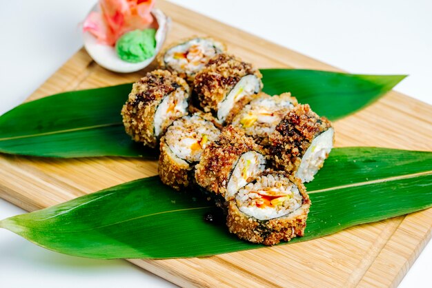 Cerca de rollos de sushi calientes servidos con jengibre y wasabi en tablero de madera