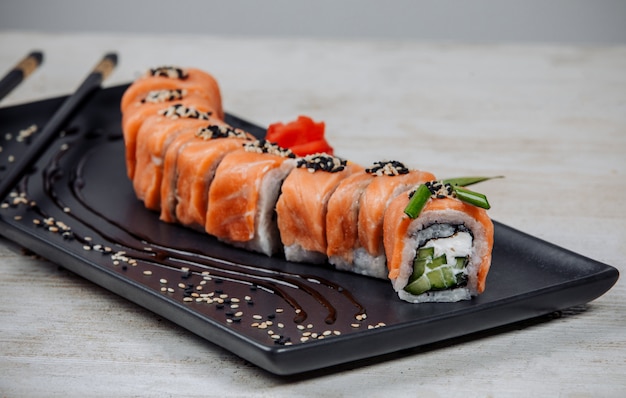 Cerca de rollos de sushi conjunto cubierto de salmón con pepino y crema