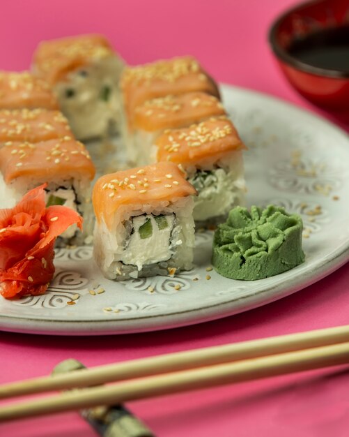 Cerca de rollos de sushi cubiertos de salmón servido con wasabi nad jengibre