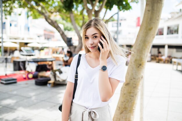 Cerca de sonriente chica atractiva hablando por teléfono mientras está parado al aire libre en una calle de la ciudad