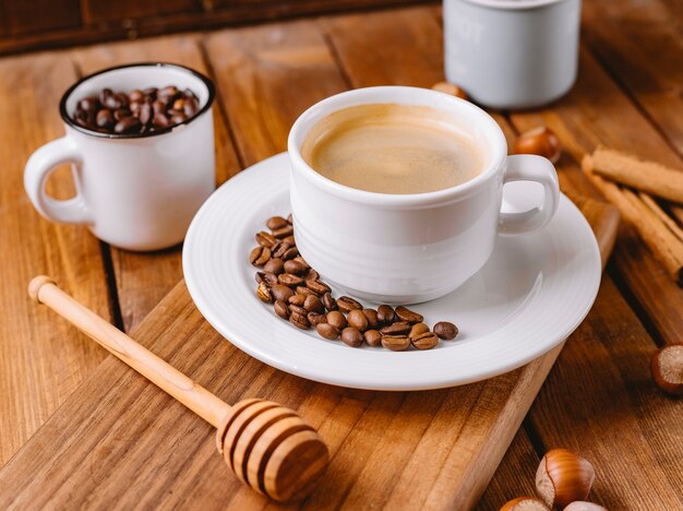 Cerca de la taza de café decorada con granos de café colocados en una tabla de servir de madera