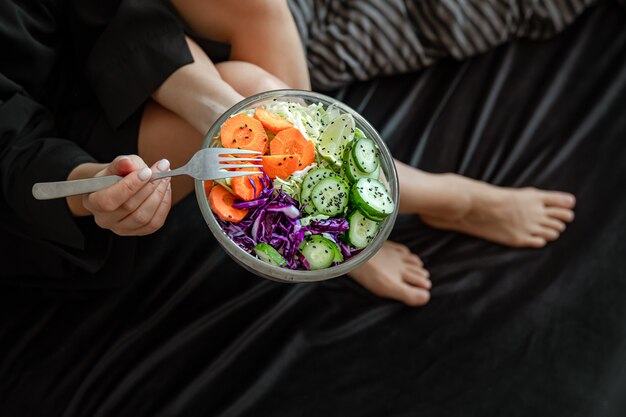 Cerca de un tazón grande con ensalada de verduras recién preparada en manos femeninas.