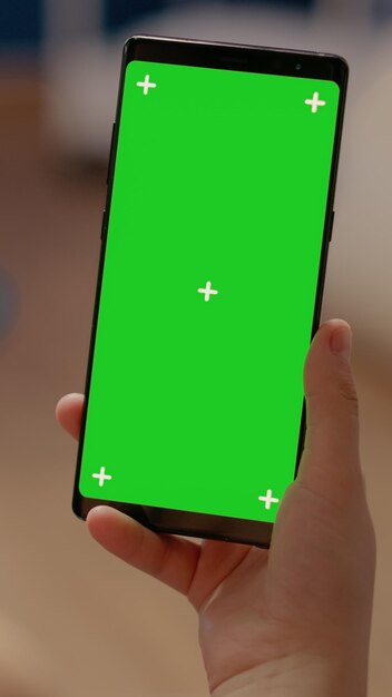 De cerca en el teléfono móvil con pantalla verde vertical utilizada para tecnología moderna y espacio de copia en blanco con plantilla de maqueta. Mujer sosteniendo dispositivo con fondo aislado y clave de croma