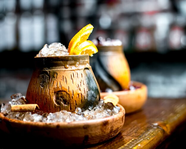 Cerca de vaso de bebida de madera con hielo jengibre y rodaja de naranja