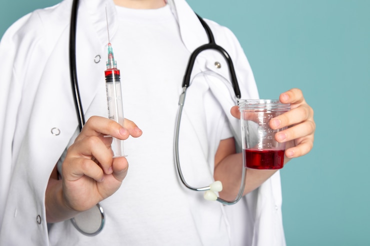 Foto gratuito de cerca, ver niño pequeño niño lindo adorable dulce con inyección y líquido rojo en traje médico blanco sobre pared azul
