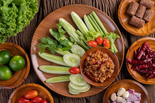 Cerdo dulce en un tazón de madera con pepino, frijoles largos, tomates y guarniciones.