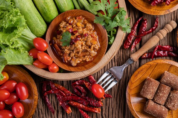 Cerdo dulce en un tazón de madera con pepino, frijoles largos, tomates y guarniciones.