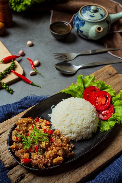 Cerdo salteado, sal y chiles, decorado con ingredientes de comida tailandesa.