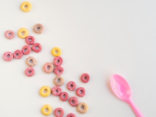 Cereal de frutas bucles y cuchara sobre fondo blanco.