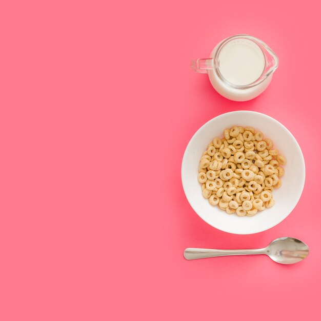 Cereales en un tazón de cerámica con leche y cuchara sobre fondo rosa