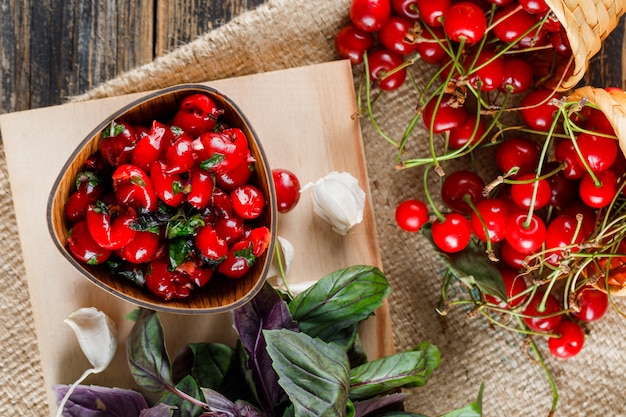 Cereza en cestas con ajo, mermelada, albahaca, tabla para cortar en madera y saco