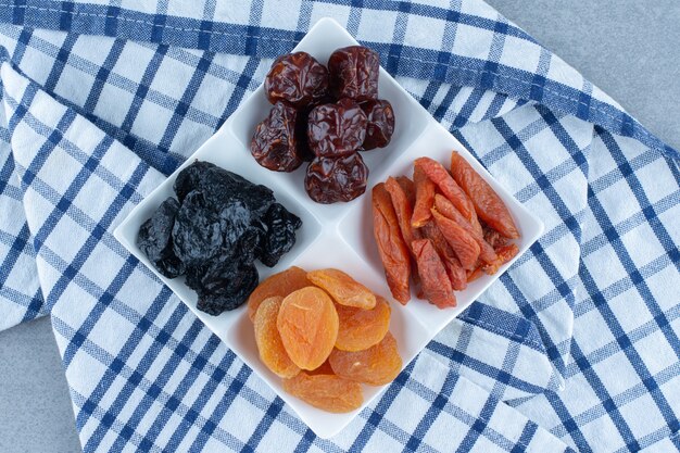 Cereza seca, albaricoque, ciruela en el cuenco, en el paño de cocina, en la mesa de mármol.