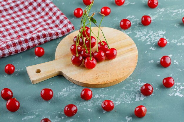 Cereza con toalla de cocina vista de ángulo alto en yeso y tabla de cortar