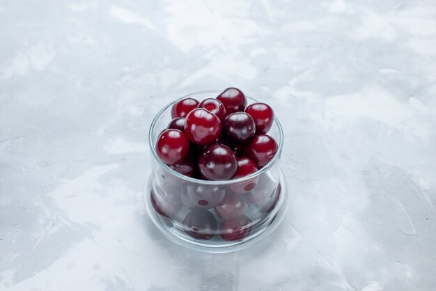 Cerezas ácidas frescas dentro de un pequeño vaso de vidrio sobre un escritorio blanco claro