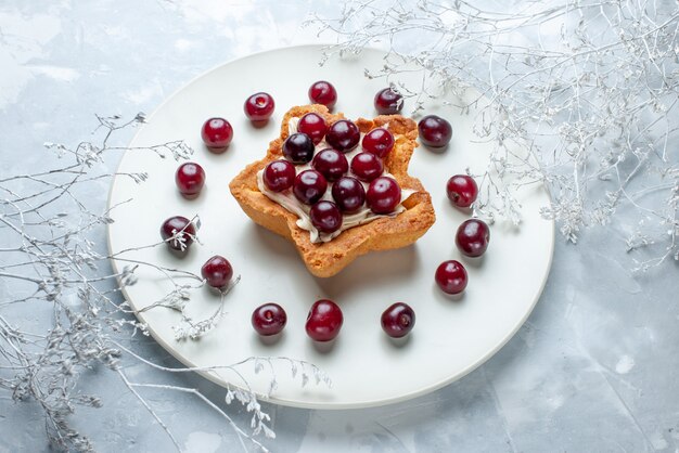 Cerezas agrias frescas dentro de la placa con pastel cremoso en forma de estrella sobre gris