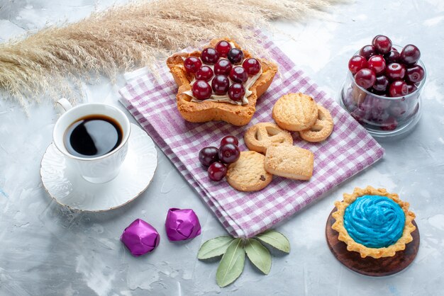 Cerezas agrias frescas dentro de la placa con pastel cremoso en forma de estrella, té y galletas en la luz