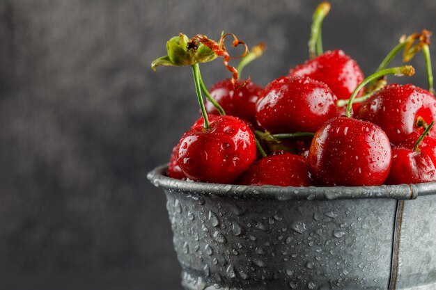 Cerezas cubiertas de rocío en un cubo de metal de cerca en una mesa gris sucio