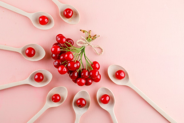 Foto gratuita cerezas en cucharas de madera en espacio rosado, plano.