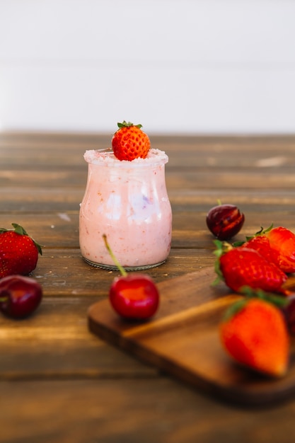 Cerezas y fresas en la tabla de cortar en frente del batido