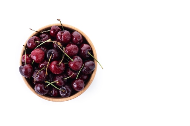 Cerezas frescas con gotas de agua en un recipiente de madera aislado sobre fondo blanco.