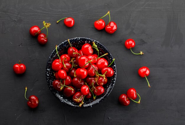 Cerezas frescas en un plato negro sobre una mesa oscura. vista superior.