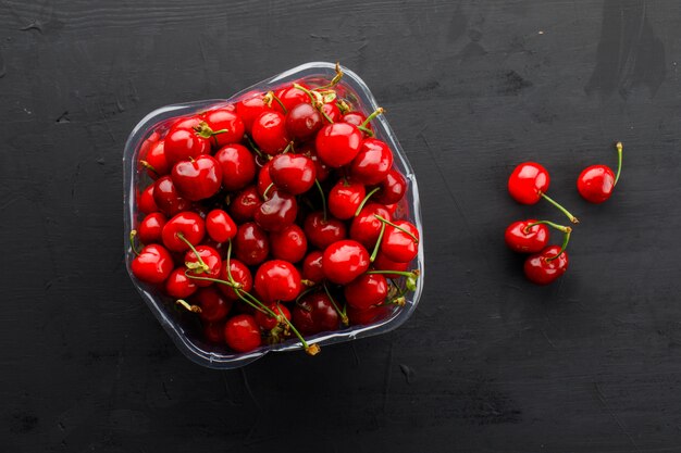 Cerezas frescas en un plato de vidrio plano yacían sobre una mesa de yeso negro